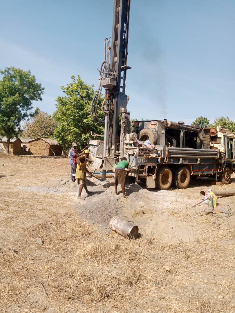 IMG-20251228-WA0003 - Wasser für Afrika - Wasser für Afrika Mobile drilling rig on a truck being operated by several workers in a dusty rural field.